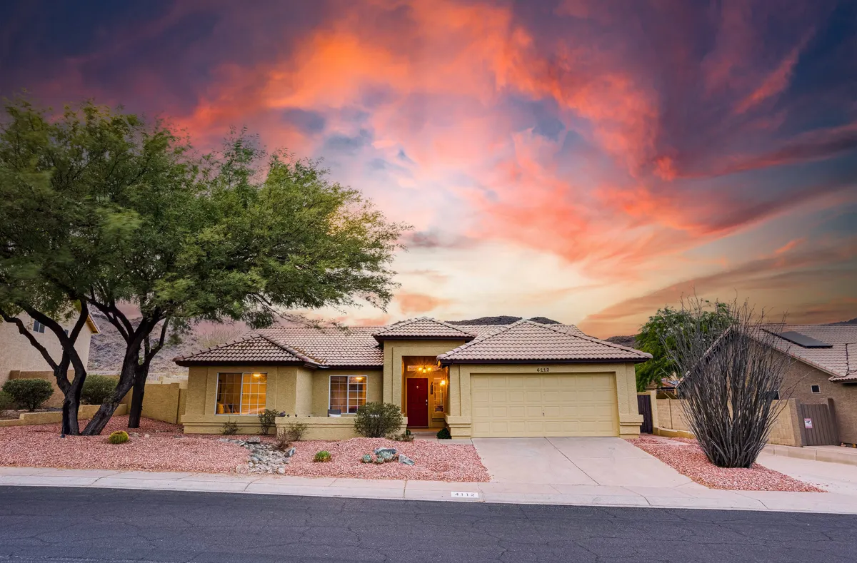 A welcoming front door framed by lush landscaping and a captivating sunset sky. The entryway is both inviting and picturesque, suggesting a warm welcome home and the beauty of evenings spent outdoors.