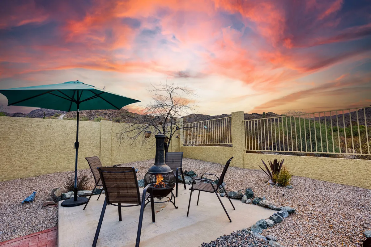 An inviting fire pit is surrounded by comfortable chairs and an umbrella, all set against a vivid sunset sky. This cozy scene embodies the perfect setting for evening storytelling, s'mores, and stargazing, bringing the 'Backyard Bliss' theme full circle.