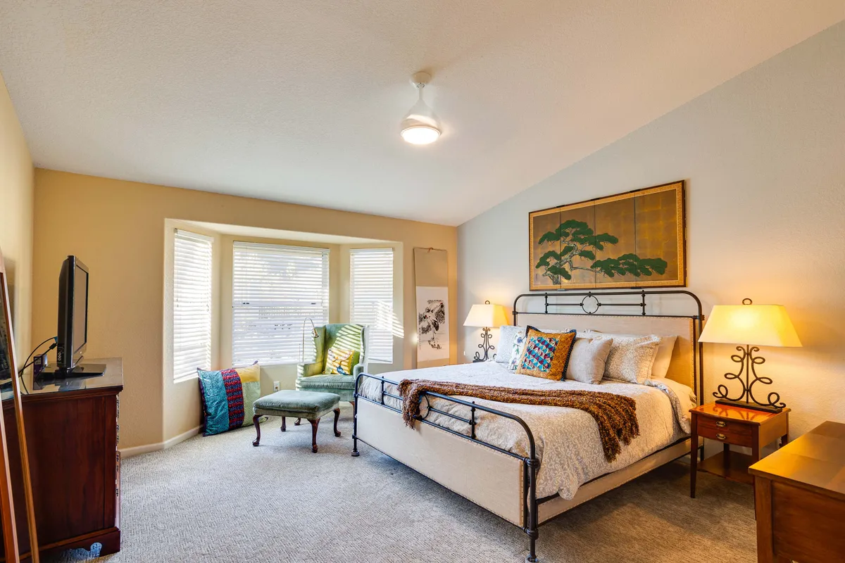 A serene bedroom with a plush bed dressed in premium linens, a window seating area perfect for a reading nook, a tasteful art piece above the bed, and a nightstand with a lamp. The room feels peaceful and inviting, ideal for restful sleep and private downtime.