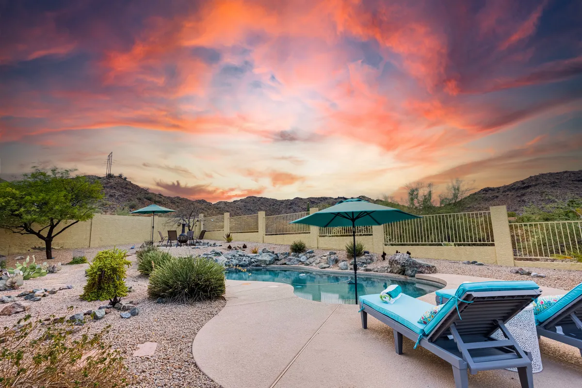 A view of the swimming pool bordered by lounge chairs and an umbrella, set against a backdrop of mountains and a landscaped garden. The scene captures a tranquil moment at sunset, with soft lighting and inviting outdoor spaces for relaxation or socializing.
