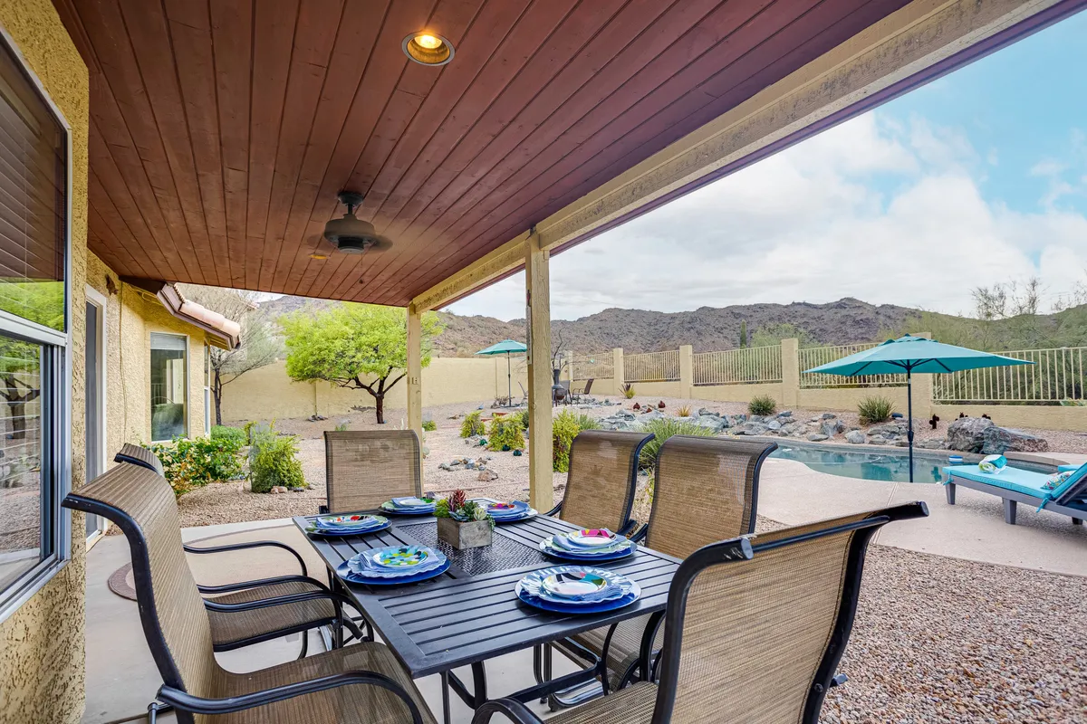 This scene presents an outdoor dining table set near the swimming pool, with green umbrellas providing shade and mountains visible in the background. The setup is ideal for alfresco meals and social gatherings, offering a seamless connection to nature and the pool area.