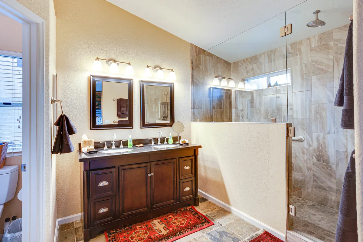 A spa-like bathroom showcasing a sleek walk-in shower, double vanity with mirrors, and a decorative rug. The space feels elegant and serene, inviting guests to unwind and enjoy a luxurious bathing experience.