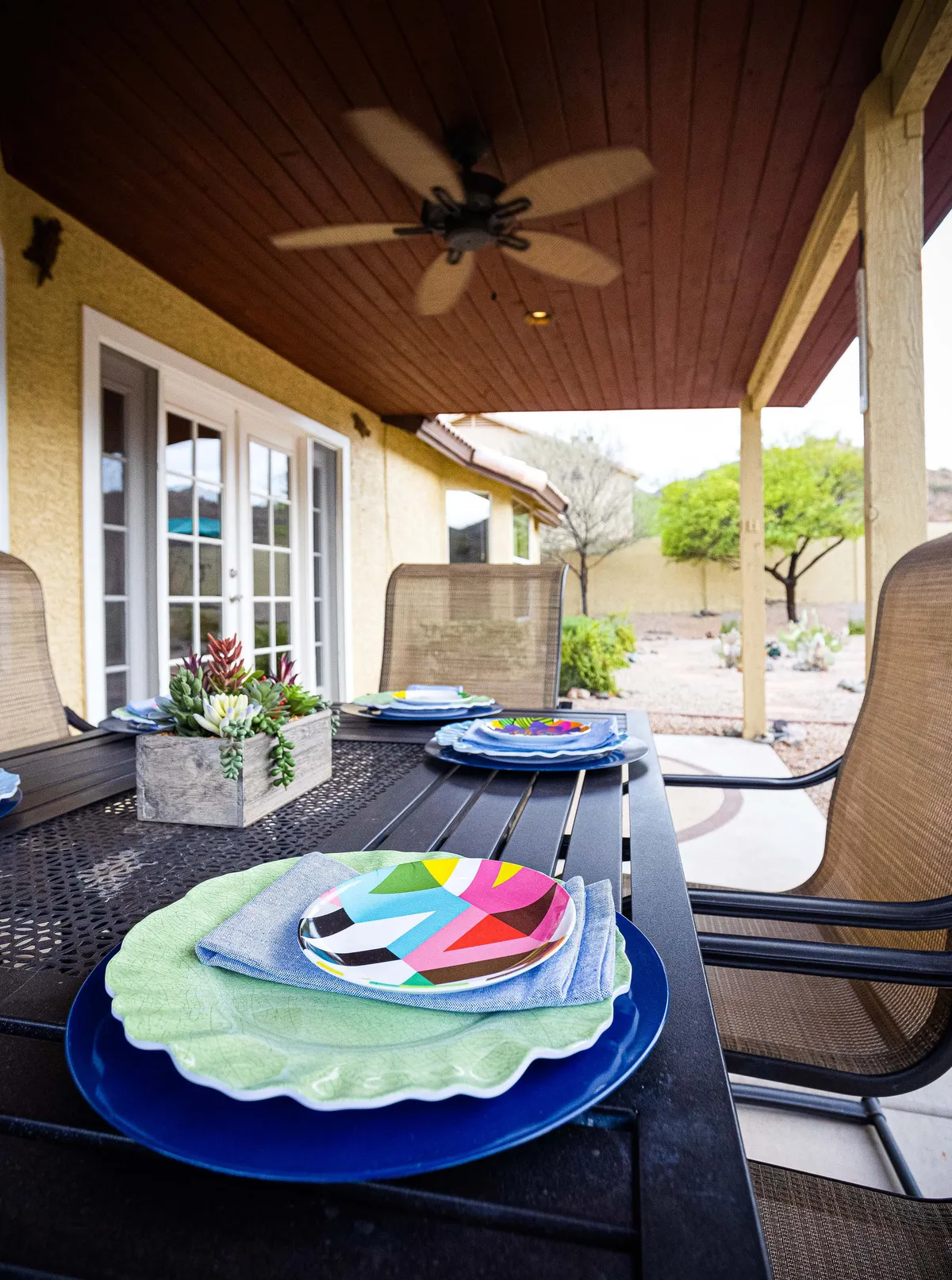 An inviting outdoor dining area with a colorful table setting, potted succulents, and ample seating. The table is set for a joyful meal, and the scene is framed by natural desert greenery, evoking a sense of cheerful togetherness and al fresco dining.