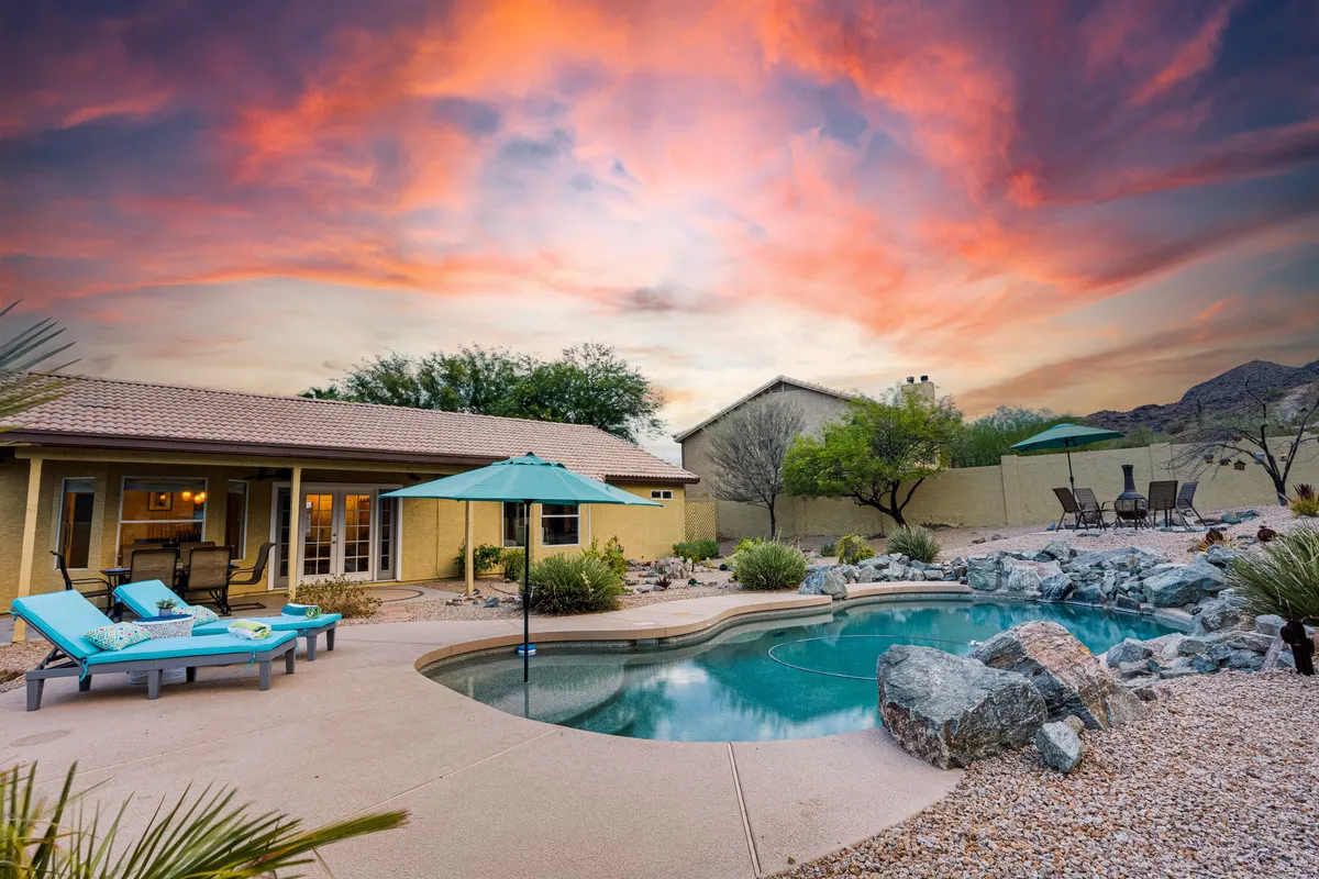 A tranquil backyard scene with a sparkling unheated swimming pool surrounded by lounge chairs and an umbrella. Rock landscaping blends seamlessly with the untouched natural preserve and mountains in the background, creating a private oasis perfect for relaxing or watching the sunset.